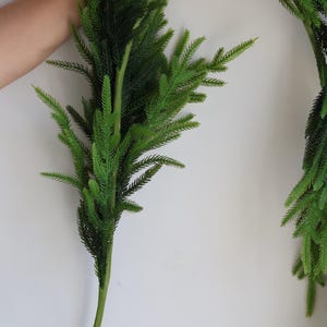 May include: A long, green artificial garland made of pine branches. The garland is flexible and can be shaped into a circle or other forms. It is perfect for adding a touch of greenery to your home decor.