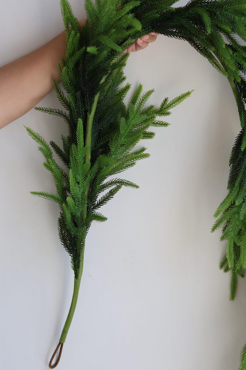 May include: A long, green artificial garland made of pine branches. The garland is flexible and can be shaped into a circle or other forms. It is perfect for adding a touch of greenery to your home decor.
