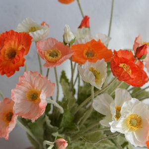 May include: A bouquet of artificial poppies in shades of orange, pink, and white. The flowers have delicate petals and are arranged in a vase.