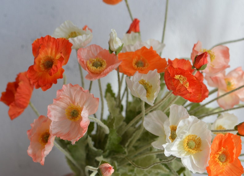 May include: A bouquet of artificial poppies in shades of orange, pink, and white. The flowers have delicate petals and are arranged in a vase.
