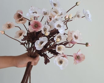 Puede incluir: Un ramo de flores de amapola artificiales en tonos blancos y rosados. Las flores tienen pétalos delicados y están dispuestas en tallos marrones.