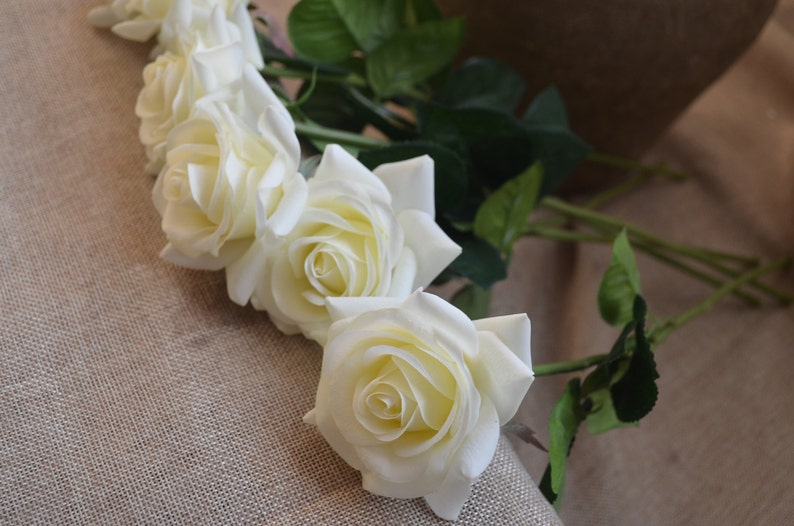 May include: A bouquet of five white artificial roses with green stems and leaves.