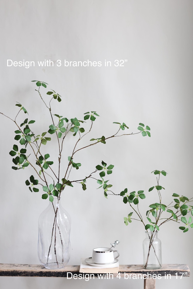Puede incluir: Dos arreglos de vegetaci&oacute;n artificial en jarrones de vidrio transparente. El arreglo m&aacute;s grande tiene tres ramas y mide 81 cm de alto. El arreglo m&aacute;s peque&ntilde;o tiene cuatro ramas y mide 43 cm de alto. "Design with 3 branches in 32" y "Design with 4 branches in 17" est&aacute;n escritos debajo de los arreglos.