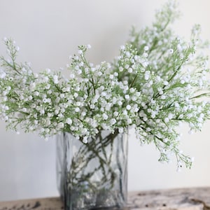 Op de afbeelding: Een boeket witte gipskruidbloemen in een heldere glazen vaas. De bloemen zijn losjes en natuurlijk gerangschikt.