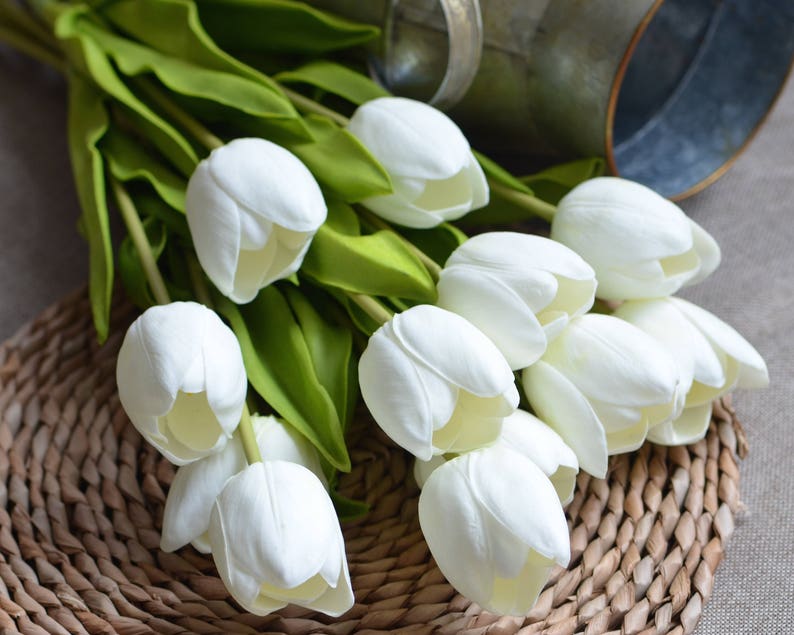 May include: A bouquet of white artificial tulips with green stems and leaves. The tulips are arranged in a woven basket.