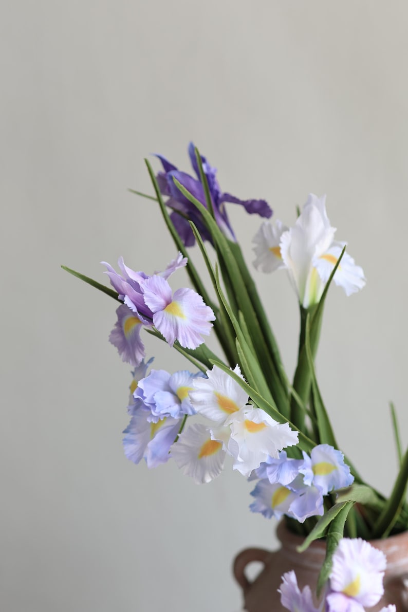 May include: A bouquet of purple, white and blue iris flowers in a brown ceramic vase. The flowers have yellow centres and are arranged in a loose, natural style.