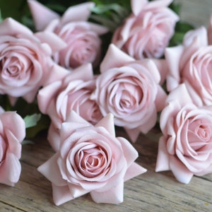 May include: A bouquet of blush pink artificial roses arranged on a wooden surface. The roses are made of fabric and have a realistic appearance.