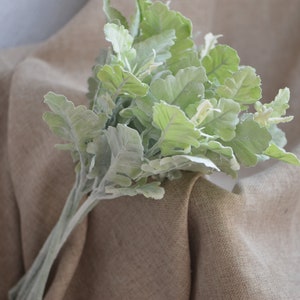 May include: A bunch of artificial lamb's ear plants with soft, fuzzy, light green leaves. The plants are arranged in a bouquet and are sitting on a brown fabric surface.