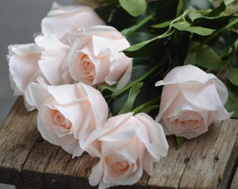 Peut inclure: Un bouquet de cinq roses rose pâle avec des tiges et des feuilles vertes. Les roses sont disposées sur une surface en bois rustique.