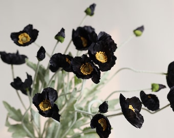 May include: A bouquet of black poppy flowers with yellow centers. The flowers are arranged in a hand-held bouquet.