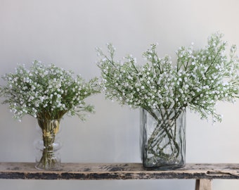 May include: Two glass vases filled with white baby's breath flowers on a rustic wooden shelf.