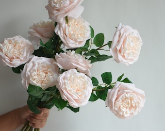 May include: A bouquet of blush pink artificial roses with green leaves. The roses have a layered, ruffled appearance.