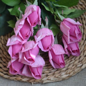 May include: A bouquet of pink artificial roses arranged on a woven wicker surface.