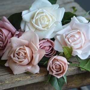 Op de afbeelding: Een boeket kunstmatige rozen in roze en witte tinten. De rozen zijn gerangschikt op een rustiek houten oppervlak.