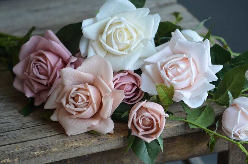 Op de afbeelding: Een boeket kunstmatige rozen in roze en witte tinten. De rozen zijn gerangschikt op een rustiek houten oppervlak.