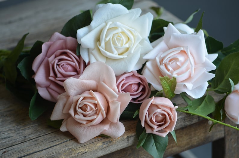 Op de afbeelding: Een boeket kunstmatige rozen in roze en witte tinten. De rozen zijn gerangschikt op een houten oppervlak.