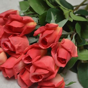 Puede incluir: Un ramo de rosas rojas artificiales con hojas verdes. Las rosas est&aacute;n dispuestas en un racimo, con los tallos apuntando en diferentes direcciones.