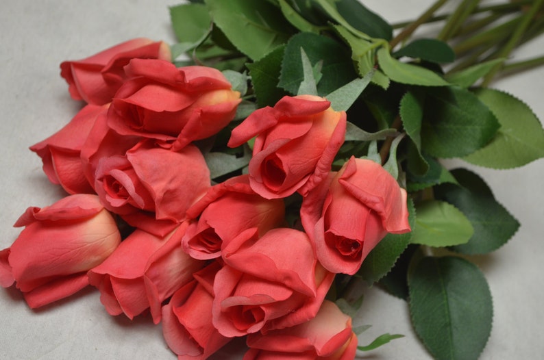 Puede incluir: Un ramo de rosas rojas artificiales con hojas verdes. Las rosas est&aacute;n dispuestas en un racimo, con los tallos apuntando en diferentes direcciones.