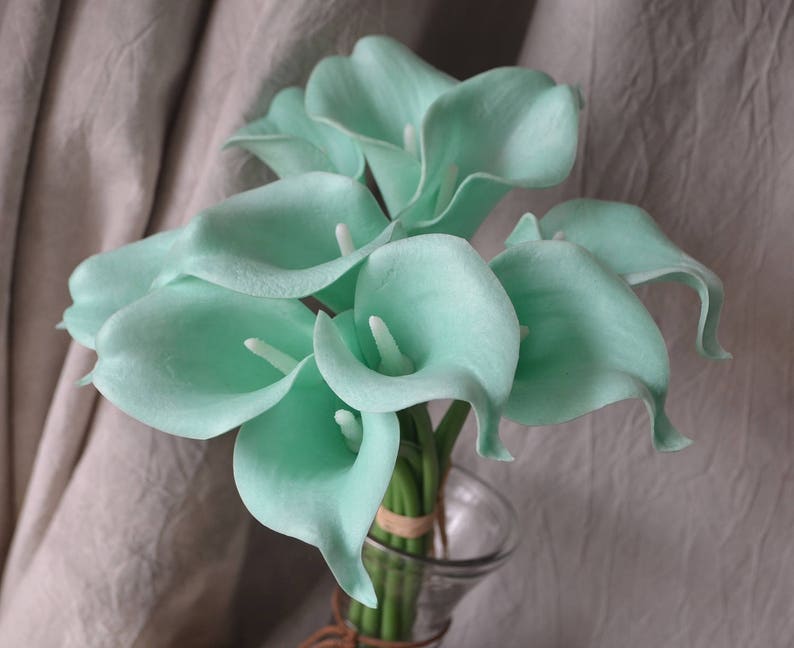 May include: A bouquet of light green calla lilies arranged in a clear glass vase. The lilies are in full bloom and have a delicate, elegant appearance.