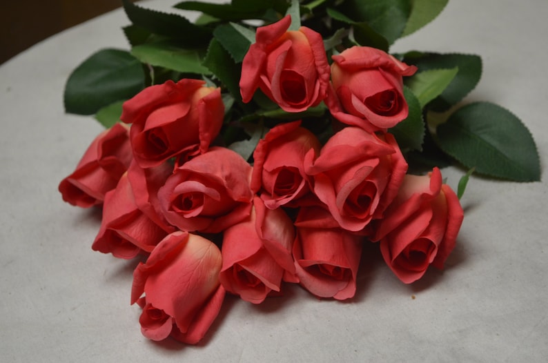 Puede incluir: Un ramo de rosas de seda rojas con hojas verdes. Las rosas est&aacute;n dispuestas en un racimo, con los tallos apuntando hacia arriba.