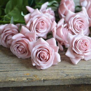 May include: A bouquet of pale pink roses arranged on a rustic wooden surface. The roses are in full bloom and have a soft, delicate appearance.