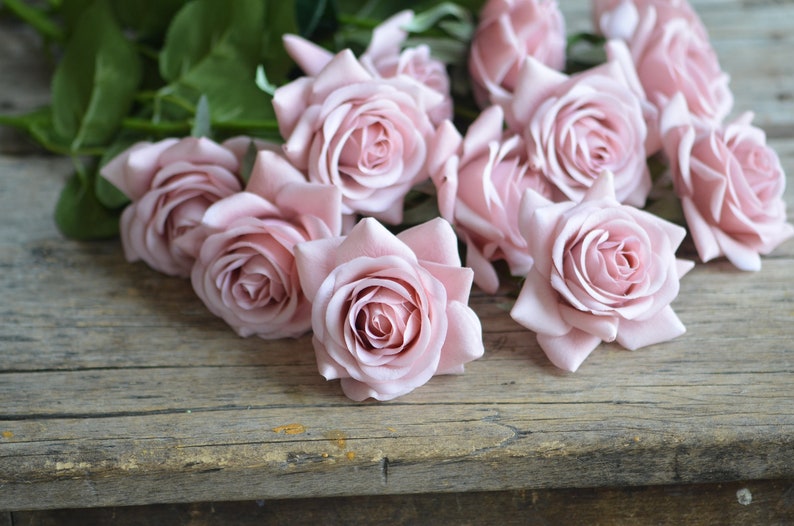 May include: A bouquet of pale pink roses arranged on a rustic wooden surface. The roses are in full bloom and have a soft, delicate appearance.