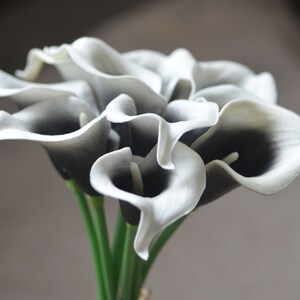 May include: A bouquet of artificial calla lilies with white petals and black centers. The stems are green.