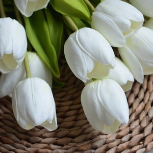 May include: A bouquet of white artificial tulips arranged on a woven wicker surface.