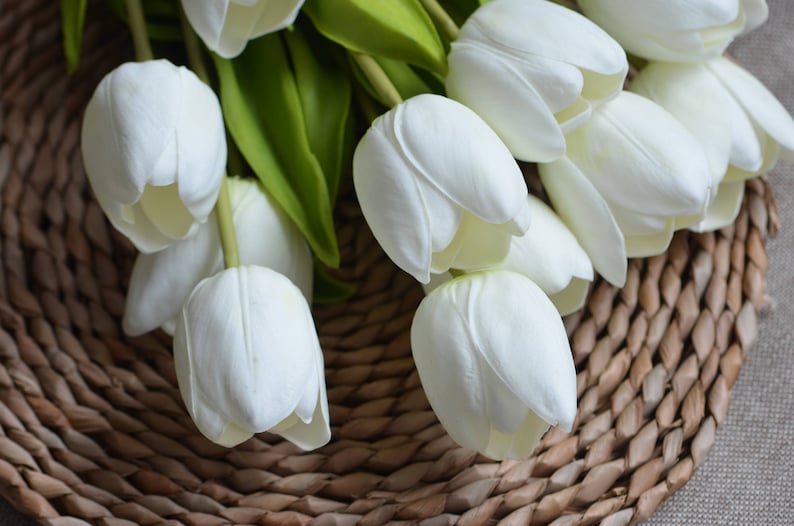 May include: A bouquet of white artificial tulips arranged on a woven wicker surface.