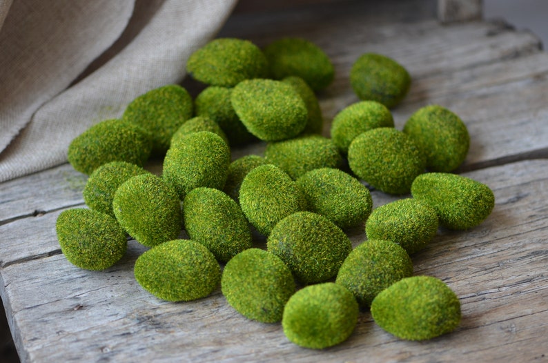May include: A collection of moss-covered stones, each with a slightly different shape and size. The stones are a vibrant green colour and are arranged on a wooden surface.