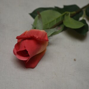 Puede incluir: Una sola rosa artificial con un degradado de melocot&oacute;n y rojo. La rosa est&aacute; sobre un fondo blanco.