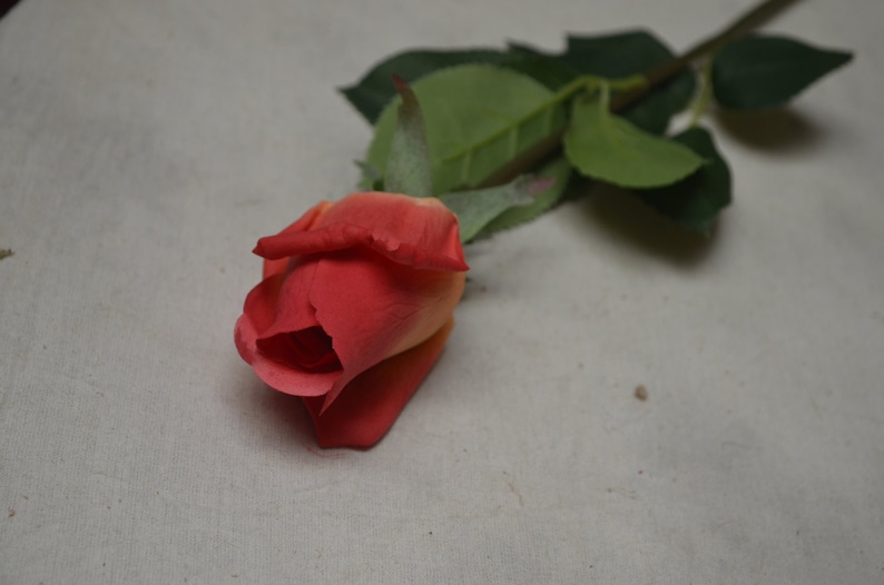 Puede incluir: Una sola rosa artificial con un degradado de melocot&oacute;n y rojo. La rosa est&aacute; sobre un fondo blanco.