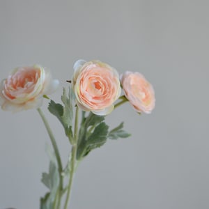 May include: A bouquet of three peach-colored artificial flowers with green leaves.