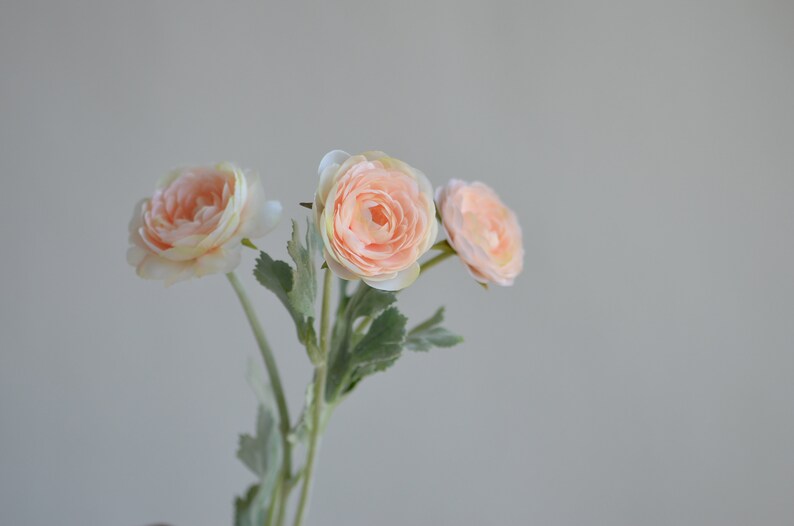 May include: A bouquet of three peach-colored artificial flowers with green leaves.