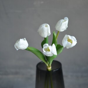 May include: A bouquet of five white tulips with green stems in a gray vase.