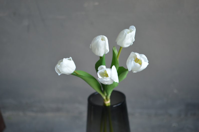 May include: A bouquet of five white tulips with green stems in a gray vase.