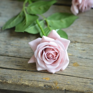 May include: A single pink rose with a green stem and leaves on a wooden surface.