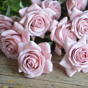May include: A bouquet of pale pink silk roses arranged on a rustic wooden surface. The roses have a soft, velvety texture and are arranged in a casual, natural style.