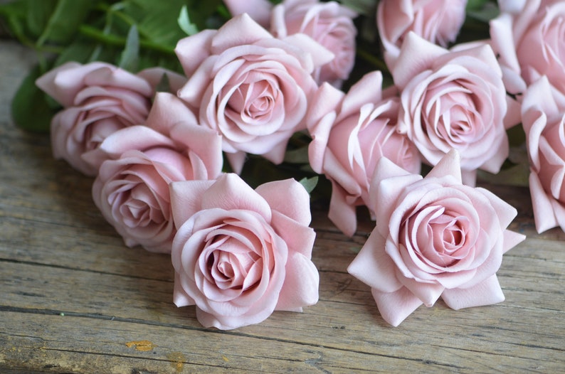 May include: A bouquet of pale pink silk roses arranged on a rustic wooden surface. The roses have a soft, velvety texture and are arranged in a casual, natural style.