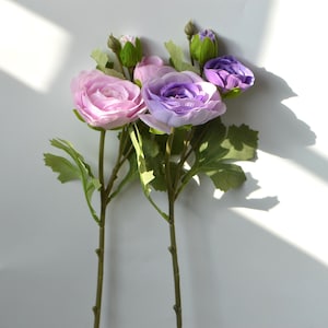 May include: A bouquet of artificial flowers with pink and purple blooms. The flowers have a delicate, layered appearance and are arranged on green stems.