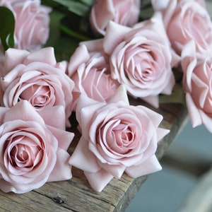 May include: A bouquet of pale pink roses with soft petals arranged on a rustic wooden surface.
