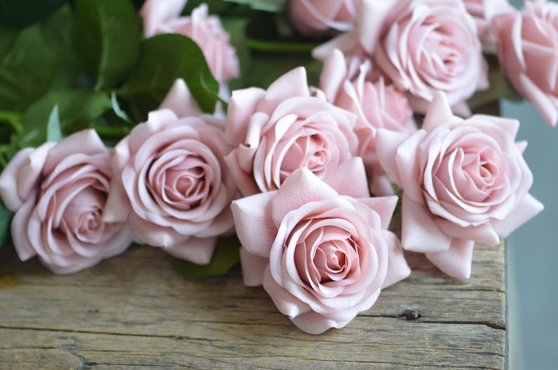May include: A bouquet of pale pink roses with soft petals, arranged on a rustic wooden surface.
