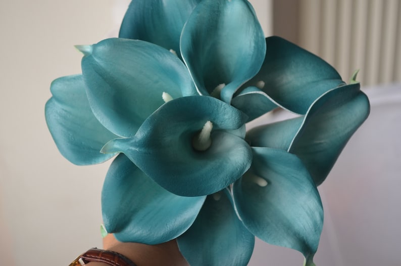 Op de afbeelding: Een boeket van teal kunstmatige calla lelies. De bloemen zijn gerangschikt in een handgehouden boeket.