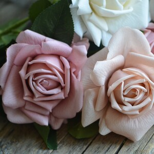 Op de afbeelding: Een boeket kunstmatige rozen in tinten roze en wit. De rozen zijn in een tros gerangschikt, met de witte roos in het midden en de roze rozen eromheen.
