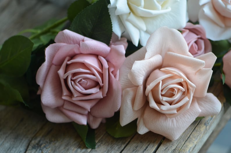 Op de afbeelding: Een boeket kunstmatige rozen in tinten roze en wit. De rozen zijn in een tros gerangschikt, met de witte roos in het midden en de roze rozen eromheen.