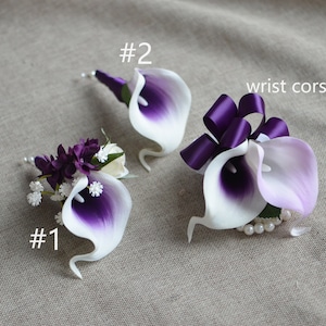 Könnte beinhalten: Drei Ansteckblumen aus weißen und violetten Calla-Lilien. Die erste Ansteckblume ist ein kleiner Strauß aus violetten Blumen mit einer einzelnen Calla-Lilie. Die zweite Ansteckblume ist eine einzelne Calla-Lilie mit einem violetten Band. Die dritte Ansteckblume ist eine einzelne Calla-Lilie mit einem Perlenarmband und einem violetten Band. Der Text "wrist corsage" ist im Bild sichtbar.