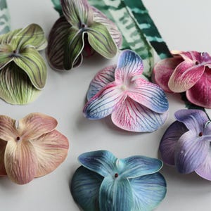 May include: Assortment of seven artificial orchid flower heads in various colors, including green, pink, blue, and purple. The flowers are made of fabric and have a realistic appearance.