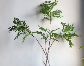 Peut inclure: Un bouquet de branches feuillues vertes artificielles dans un vase en verre transparent. Les branches ont un aspect naturel et réaliste et sont parfaites pour ajouter une touche de verdure à n'importe quel espace.