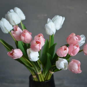 May include: A bouquet of artificial tulips in shades of pink and white. The tulips are arranged in a vase and have green stems and leaves.