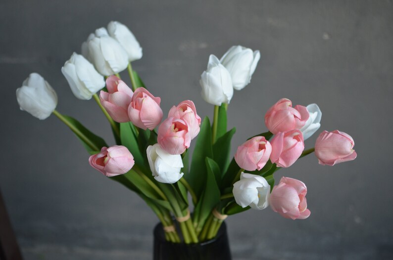 May include: A bouquet of artificial tulips in shades of pink and white. The tulips are arranged in a vase and have green stems and leaves.
